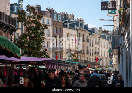 A throng of people in the street market in Grande Rue against a back-drop of typical townhouses in Dieppe, France. Stock Photo