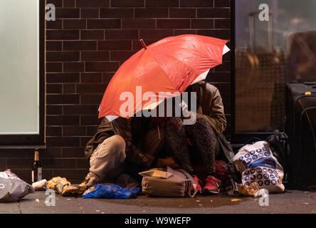 15 August 2019, Hessen, Frankfurt/Main: Two junkies have retreated under an umbrella on the edge of the station quarter night. (to dpa 'Frankfurt celebrates station quarter with big street festival') Photo: Boris Roessler/dpa Stock Photo