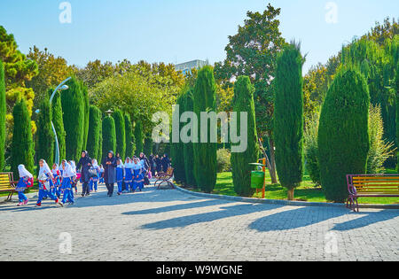 TEHRAN, IRAN - OCTOBER 25, 2017:  Iranian schoolgirls in uniforms and hijabs and their teachers walk along the thuja trees in Laleh Park, on October 2 Stock Photo