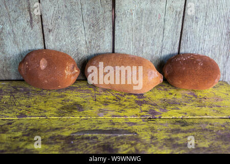 Close up of  three Cupuacu (Theobroma grandiflorum) 'Cupuaçu' fresh fruits on wooden green table background of amazon rainforest village. Stock Photo