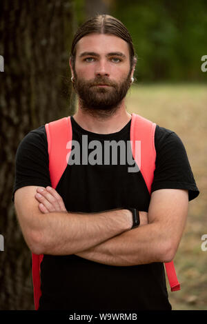 Portrait of young male in natural light looking defensive while holding his arms crossed and wearing a black shirt. Bearded caucasian man looking at t Stock Photo