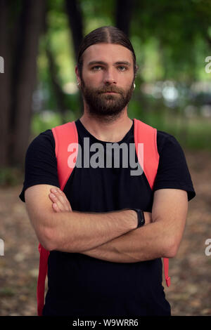 Portrait of young male in natural light looking defensive while holding his arms crossed and wearing a black shirt. Bearded caucasian man looking at t Stock Photo