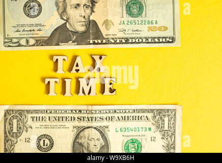 Economic phrase Tax Time isolated on yellow paper background with dollar bills. Stock Photo