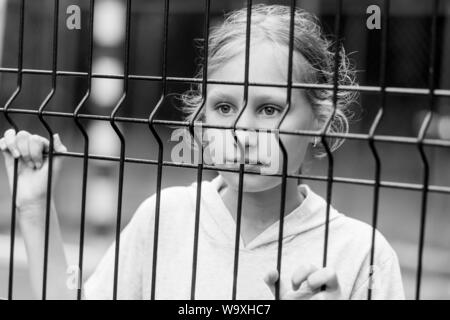 Portrait of young caucasian girl behind the net. Social issues, kid depression and sadness. Black and white shot. Stock Photo