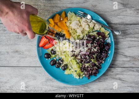 Closeup shot of a vegetable and fruit salad with a person pouring vegetable oil on it Stock Photo