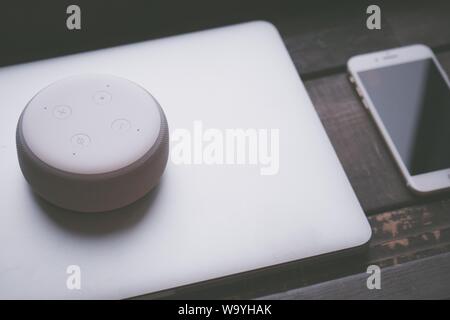 Closeup shot of a large round white Bluetooth speaker on a gray laptop and a smartphone on the side Stock Photo