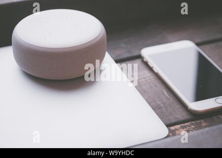 Closeup shot of a large round white Bluetooth speaker on a gray laptop and a smartphone on the side Stock Photo