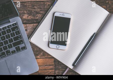 Closeup shot of a smartphone on opened textbook with a laptop on the side with a wooden background Stock Photo