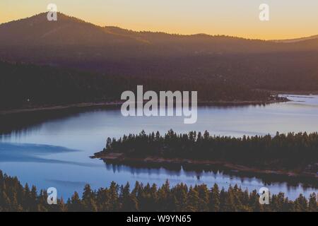 Beautiful wide shot of a lake surrounded by mountains with forests during sunset Stock Photo