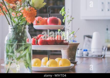 Three-level plate with apples, tomatoes, and lemons on it in the kitchen Stock Photo