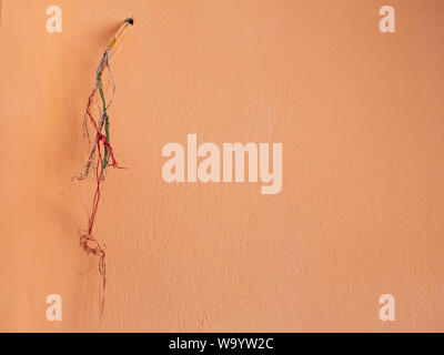 Orange wall with tangled electric wires hanging from the hole. Stock Photo