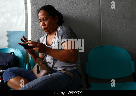 ANTIPOLO CITY, PHILIPPINES – AUGUST 9, 2019: Adult Asian woman sitting on chair using smartphone. Stock Photo