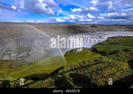 Aerial shot of a waterfall in the middle of cliffs and a rainbow over it