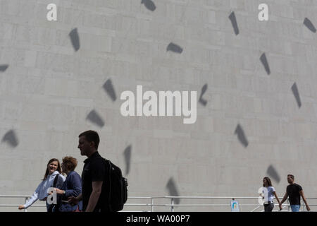 Visitors to the Southbank walk beneath the shadows of tube kites cast on an exterior concrete wall of the Royal Festival Hall on the Southbank, on 15th August, in London, England. Stock Photo