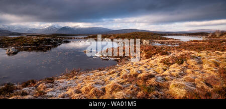 Winter ice coats Lochan na h-Achlaise lake on the vast peat bog moorland of Rannoch Moor, with the snow-capped Black Mountains in the distance. Stock Photo