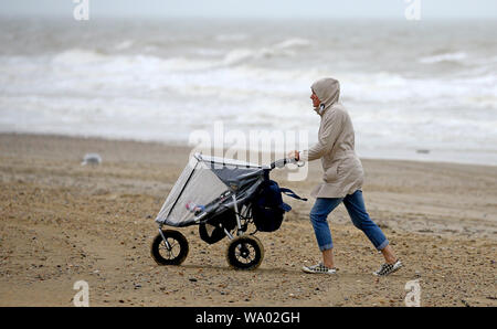 A lady pushes a buggy along Camber Sands in East Sussex during bad weather. Stock Photo