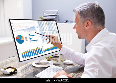 Businessman Analyzing Graphs On Computer At Workplace Stock Photo