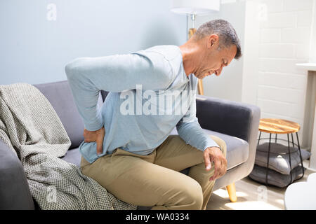 Man On Sofa Suffering From Backpain At Home Stock Photo