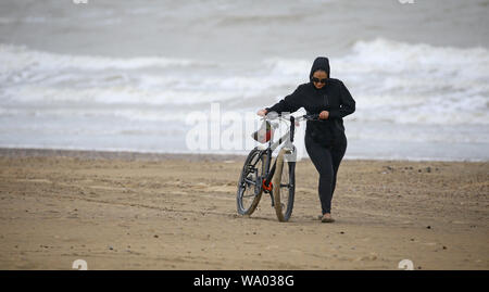 A lady pushes her bike along an empty beach in Camber, East Sussex, during bad weather. Stock Photo