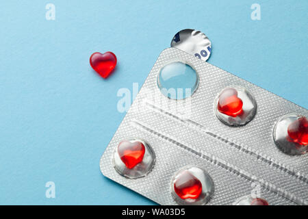 Love pills. Blister pack with red heart shaped pills. Tablets for lovers or potency. Blue background. Stock Photo