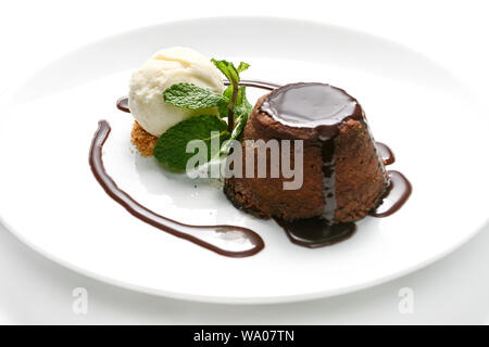 Delicious 'petit gateau' chocolate cake with cacao syrup, vanilla ice cream and mint leaf served on white plate with white background. Stock Photo