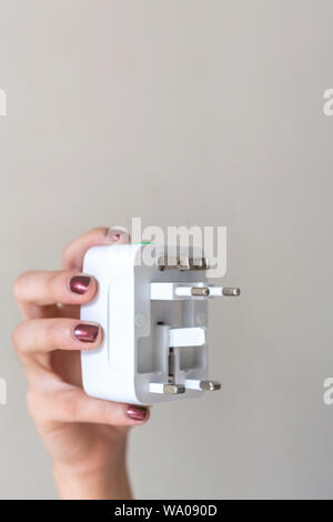Close up of woman hand holding universal electric socket plug adapters, isolated on white background. Used to connect electrical outlets worldwide. Co Stock Photo