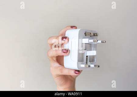 Close up of woman hand holding universal electric socket plug adapters, isolated on white background. Used to connect electrical outlets worldwide. Co Stock Photo