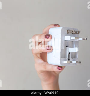 Close up of woman hand holding universal electric socket plug adapters, isolated on white background. Used to connect electrical outlets worldwide. Stock Photo