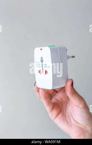 Close up of woman hand holding universal electric socket plug adapters, isolated on white background. Used to connect electrical outlets worldwide. Co Stock Photo
