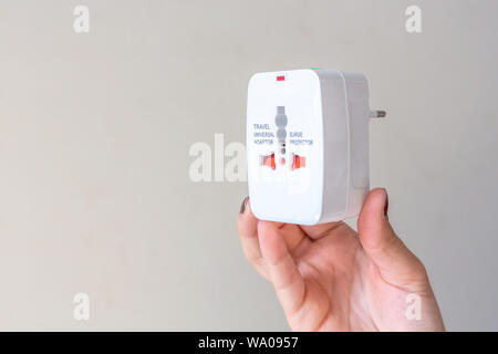 Close up of woman hand holding universal electric socket plug adapters, isolated on white background. Used to connect electrical outlets worldwide. Co Stock Photo