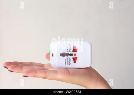 Close up of woman hand holding universal electric socket plug adapters, isolated on white background. Used to connect electrical outlets worldwide. Co Stock Photo