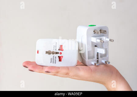 Close up of woman hand holding universal electric socket plug adapters, isolated on white background. Used to connect electrical outlets worldwide. Co Stock Photo
