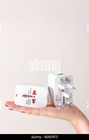 Close up of woman hand holding universal electric socket plug adapters, isolated on white background. Used to connect electrical outlets worldwide. Co Stock Photo