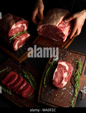 Hands of a man showing different cuts of raw beef. Low key image, vertical orientation. Stock Photo