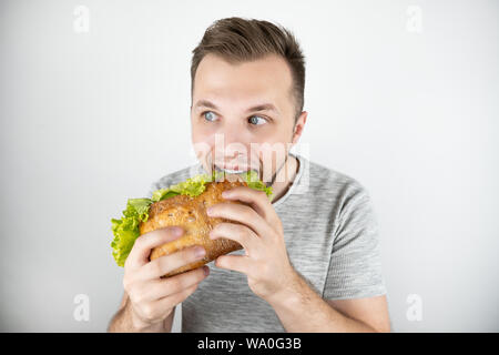 young handsome hungry man biting fresh sandwich with salad leaf on isolated white background. Stock Photo