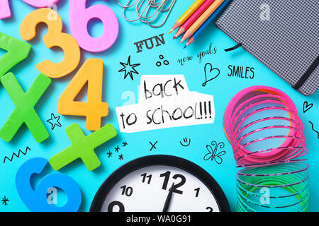 a clock, some pencil crayon of different colors, a notepad, some paper clips, some numbers of different colors, some drawings and the text back to sch Stock Photo