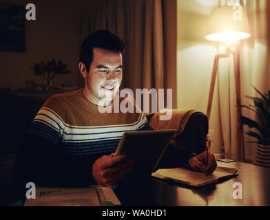 Happy man working late at night at home office using digital tablet Stock Photo