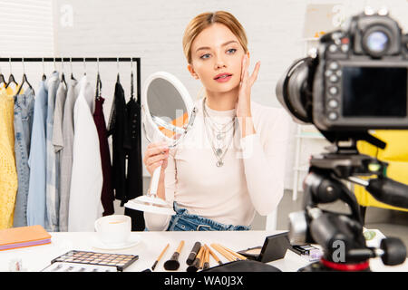 beauty blogger holding mirror and touching face in front of video camera Stock Photo