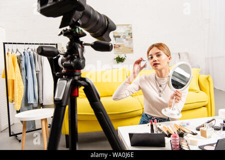 beauty blogger holding mirror and curling eyelashes in front of video camera Stock Photo