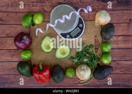 Top overhead view of fresh guacamole ingredients with weight scale and measuring tape. Avocado cut in half, fresh cilantro, red bell pepper, green lim Stock Photo