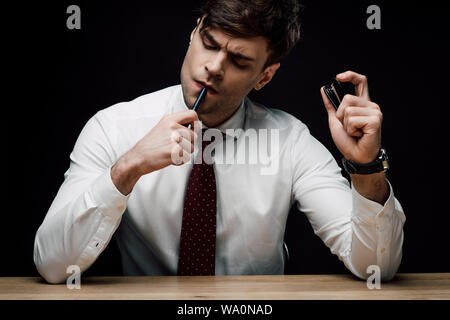 thoughtful businessman holding stapler and pen isolated on black Stock Photo
