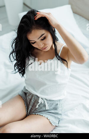 overhead view of thai woman touching hair while sitting on bed Stock Photo