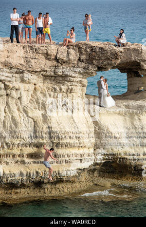 People standing and sitting on the rocks, enjoying the crystal clear waters and a young married couple get photography Stock Photo