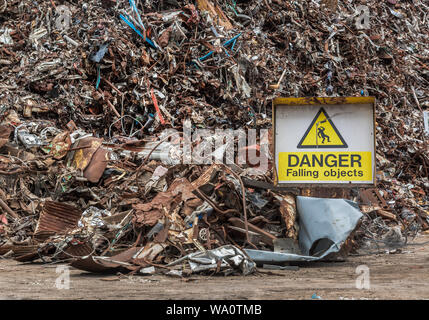 A yellow danger sign in front of a huge heap of scrap metal. Stock Photo