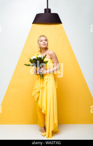 attractive young woman holding bouquet of flowers on white and yellow Stock Photo