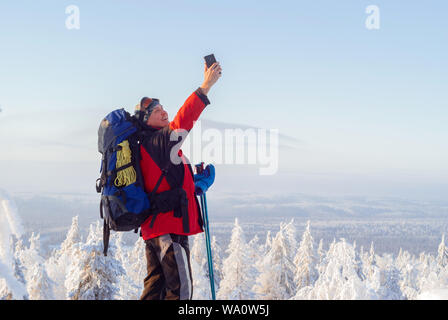 hiker on top of a mountain in winter catches a signal by raising his hand with a smartphone up, or simply takes a selfie Stock Photo