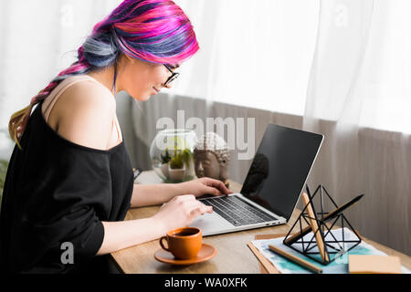 side view of girl with colorful hair sitting at desk and using laptop Stock Photo