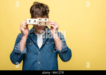 young man in denim shirt showing wooden cubes with fake fact lettering on yellow background Stock Photo
