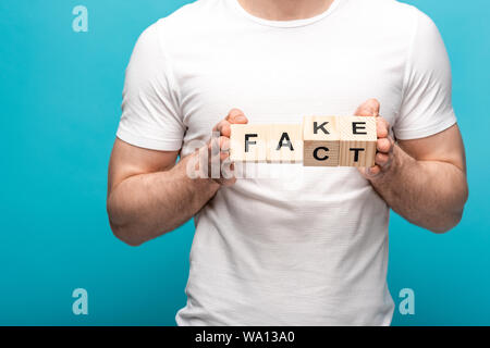 partial view of man in white t-shirt holding wooden cubes with fake fact lettering on blue background Stock Photo