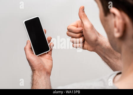 partial view of man showing thumb up while holding smartphone with blank screen isolated on grey Stock Photo